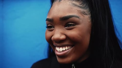 One young black hispanic woman smiling on blue wall, close-up face of a 20s millennial girl of
