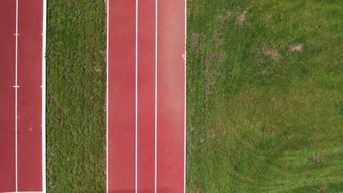 Drone top down pan across empty red rubber of track lined with mowed grassy field