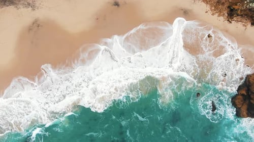 Luftaufnahme eines abgelegenen Sandstrandes mit türkisfarbenen Wellen, die gegen die Küste prallen, umgeben von