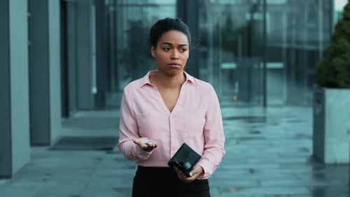 Woman Standing Outside an Office Building Holding a Wallet and Looking Thoughtful