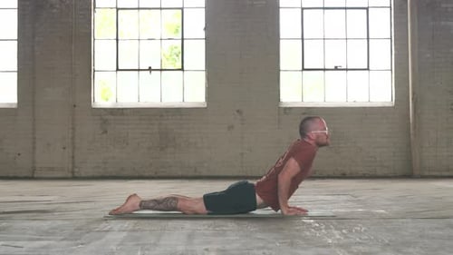 Mann in einer Industriehalle praktiziert Yoga, die Pose vom Brett zum aufwärts gerichteten Hund.