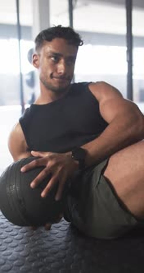 Vertical video: Exercising in gym, man doing sit-ups with medicine ball on mat