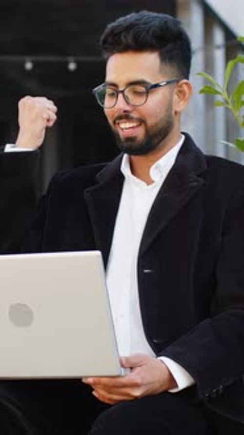 Young Man Celebrates Success with Laptop Outdoors