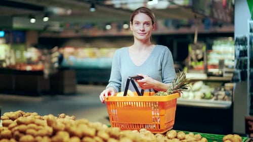 portrait of a young happy female shopper in a grocery store with a basket full of groceries. Smiling