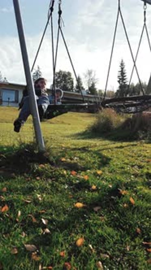 Vertical of Mother Rides Swing Nest with Son on Weekend in Countryside