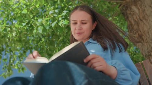 Woman Reading Book on Park Bench Outdoors