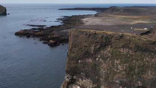 Flying past steep cliffs revealing large boulders on beach in Iceland