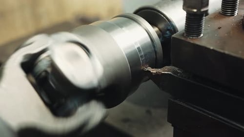 Close-up shot of turning a steel part on a lathe; metal shavings fly in different directions