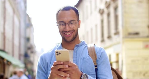 Smiling Happy and Joyful Male Traveler in Eyeglasses Chatting on Smartphone and Laughing at Street
