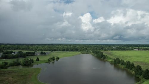 Drone footage shows a still lake close to a busy road that is surrounded by numerous trees, greenery