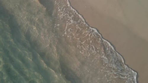 Aerial top view, medium rotating shot, small tropical wave’s break on sand beach.