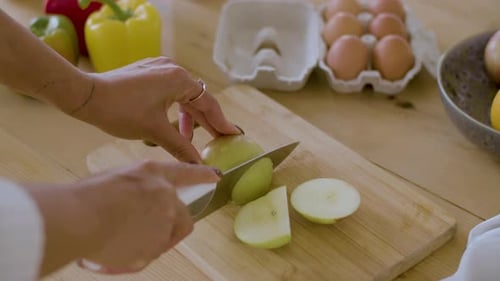 Nahaufnahme weiblicher Hände, die einen Apfel auf einem Holzbrett schneiden