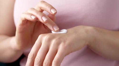 Uma mulher hidrata as mãos com creme para a pele.