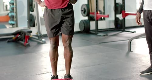 African American male trainee at gym looping band at feet performing knee raises for strength