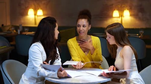 Female Friends Sitting at a Table in a Restaurant and Holding a Menu Making an Order Meeting of