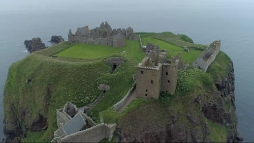 An aerial view of Dunnottar Castle on a misty and overcast day. Close-up of the castle moving right