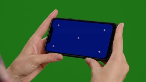 Footage with woman hands holding blue screen phone over green screen background.