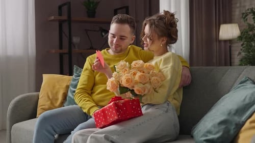 Loving Couple with Flowers and a Gift on Couch