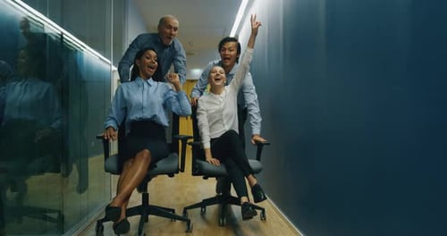 A group of carefree workers are having fun with office chairs after finishing their work.