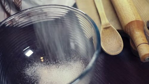 Puderzucker zum Guss, der in eine tiefe Glasschale fällt. Nudelholz