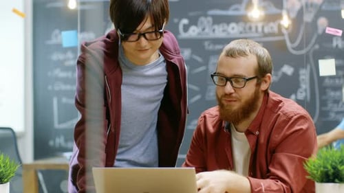 Engineer Talks with Developer About Ongoing Project while He Works on a Laptop. In the Background S