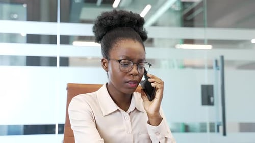 African American businesswoman talking on mobile phone while sitting at workplace in office.