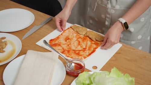 Eine Frau, die einem Lavash-Brot für einen Shawarma Hühner- und Gurkenfüllung hinzufügt