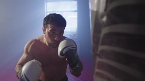 Focused Young Man Training Boxing Technique With Punching Bag