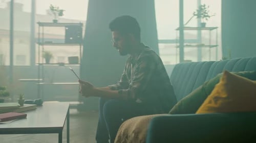 Young Adult Sitting on Couch Using Tablet Indoors