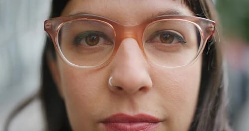 Closeup face of a woman wearing glasses to improve vision and looking serious outside on a windy