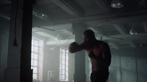 African american boxer shadow boxing in dark gym preparing for professional fight