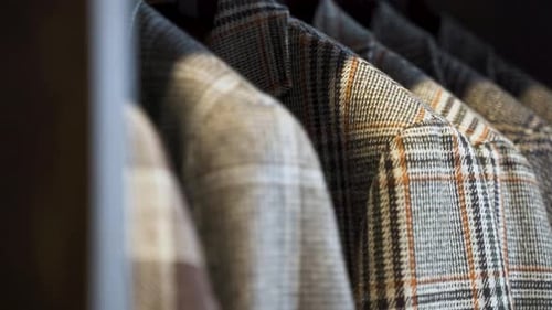 Grey patterned tweed jackets hanging in wooden wardrobe, close up.