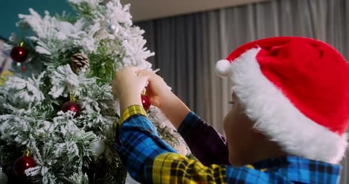 Child Decorates Snowy Christmas Tree with Red Ornaments