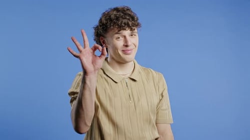 Man Gestures Okay Sign in Front of Blue Background