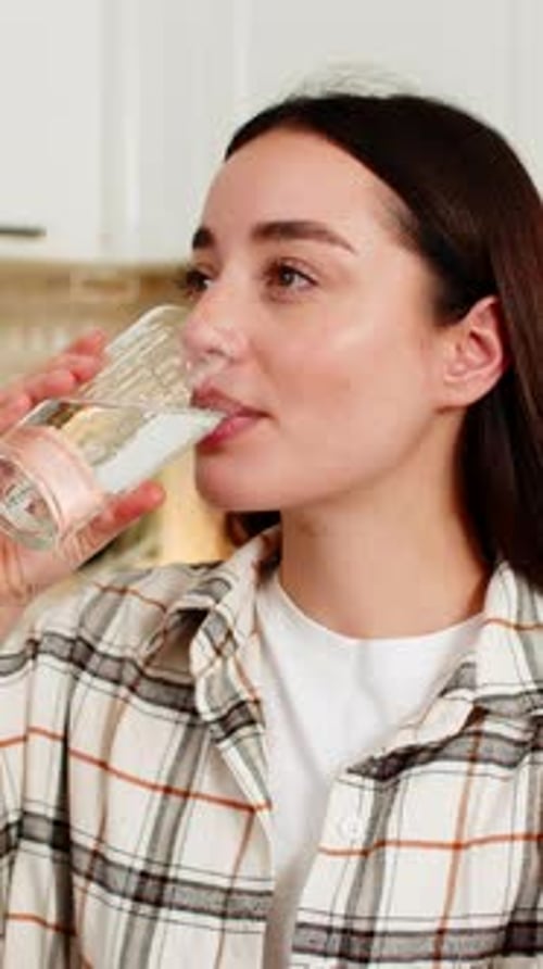 Woman Drinks Glass of Water in Bright Kitchen