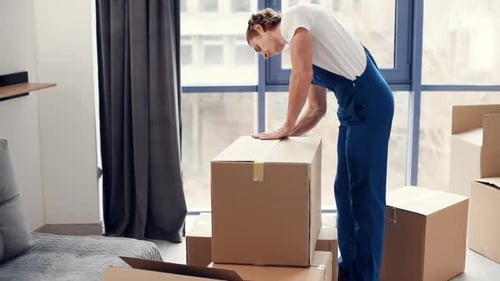 Young male mover in blue uniform works indoors in the room