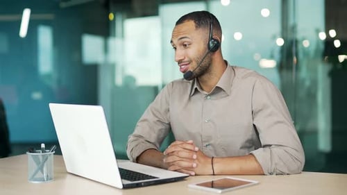 A corporate operator who works in customer support speaks on a video call using a laptop. Call