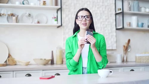Young brunette woman in green shirt eating chocolate and having toothache in the light home kitchen.