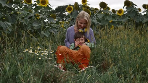 Mother and son play together on green grass next to sunflower field, Poland