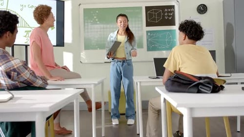 Holding tablet and speaking to classmates, teenage girl presenting in high school classroom