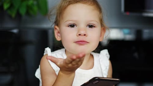 Little Girl Blows Kiss Holding Mobile Phone Indoors