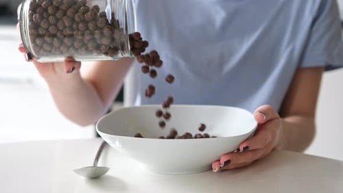 Woman Pours Chocolate Cereal into Bowl