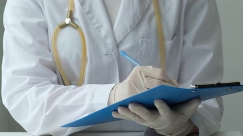 Female Doctor Filling Up Medical Form at Clipboard in Hospital Close Up