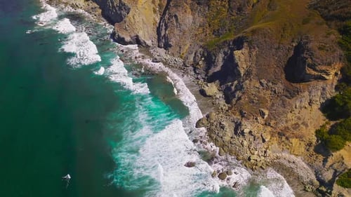 Aquamarine waters of Pacific Ocean meeting rugged craggy rocks of the California coast.