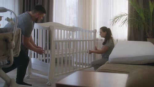 Parents Assembling White Crib for Future Baby at Nursery
