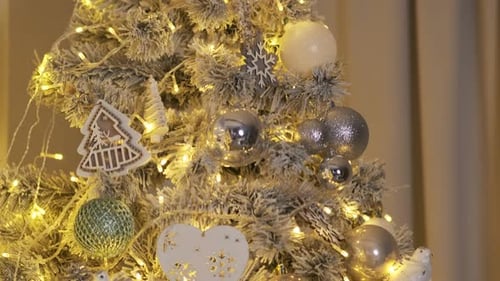 The white Christmas tree is decorated with golden toys. Warm yellow light. Celebration of new year,