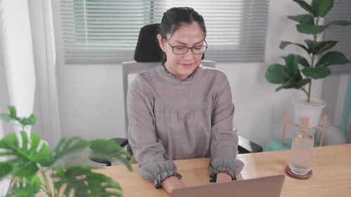 Woman sitting working at wooden table using laptop notebook looking at text typed