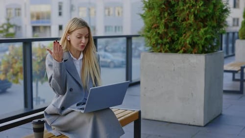 Angry Businesswoman Expressing at Laptop Video Call Sitting on the Bench Outside Near Office
