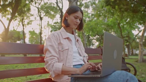 Female Freelancer Working on Laptop in Park at Sunset