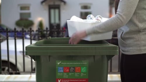 Caucasian female filling a Green Recycling Bin.